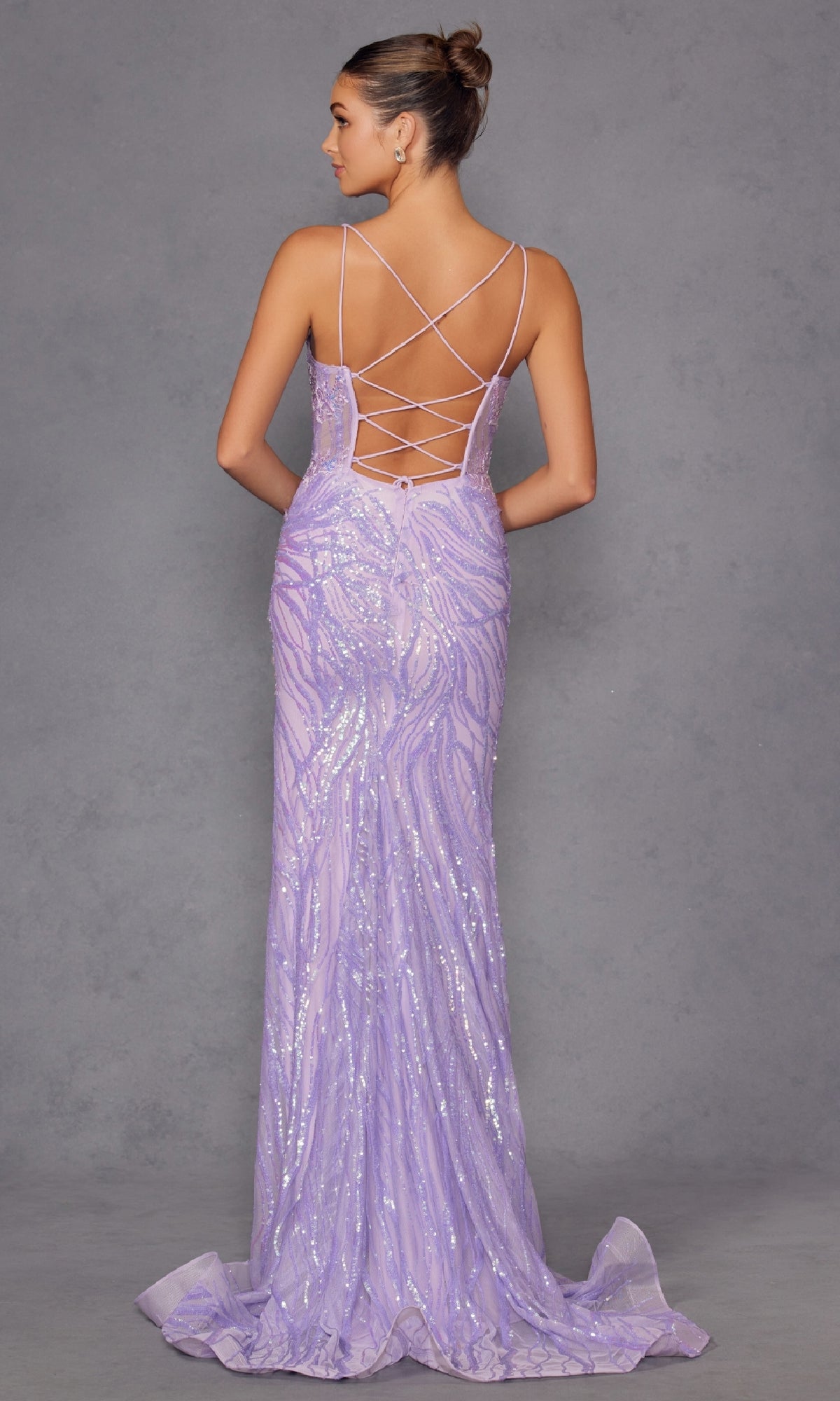 A woman faces away from the camera in the Long Lilac Sequin Prom Dress: Juliet JT2473R, featuring a floor-length silhouette and lace-up open back, standing against a plain gray background.